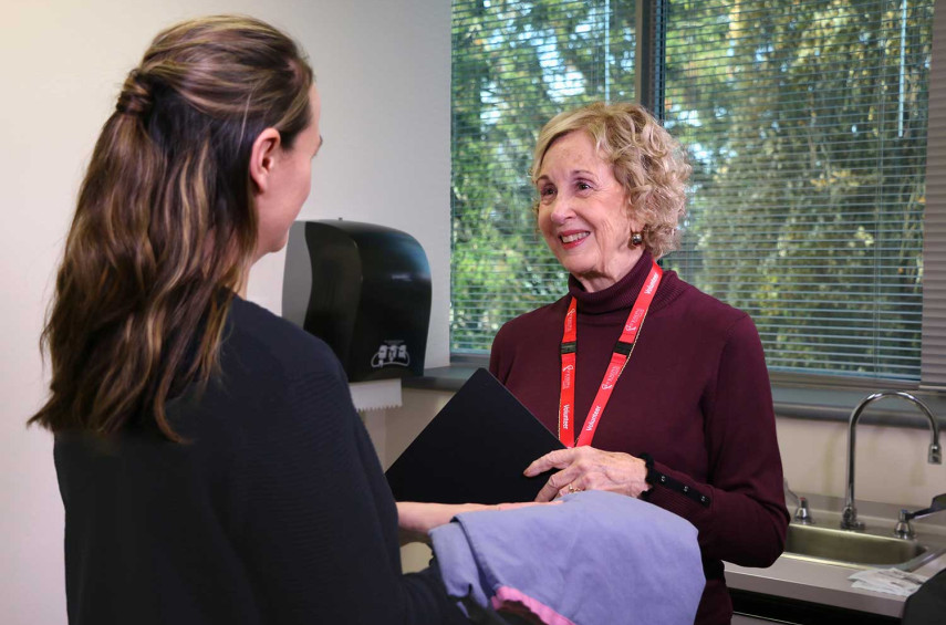 Patricia Mowry wearing a volunteer's lanyard handing a gown to a patient in the Breast Care Program